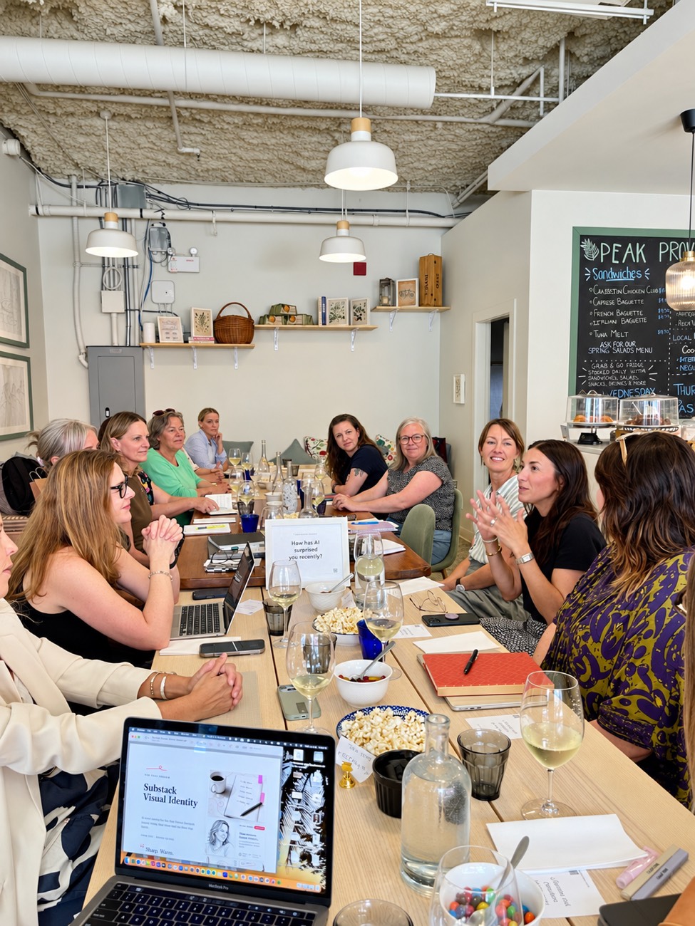 Women around a long table mid-conversation, with a printed conversation prompt standing in the centre